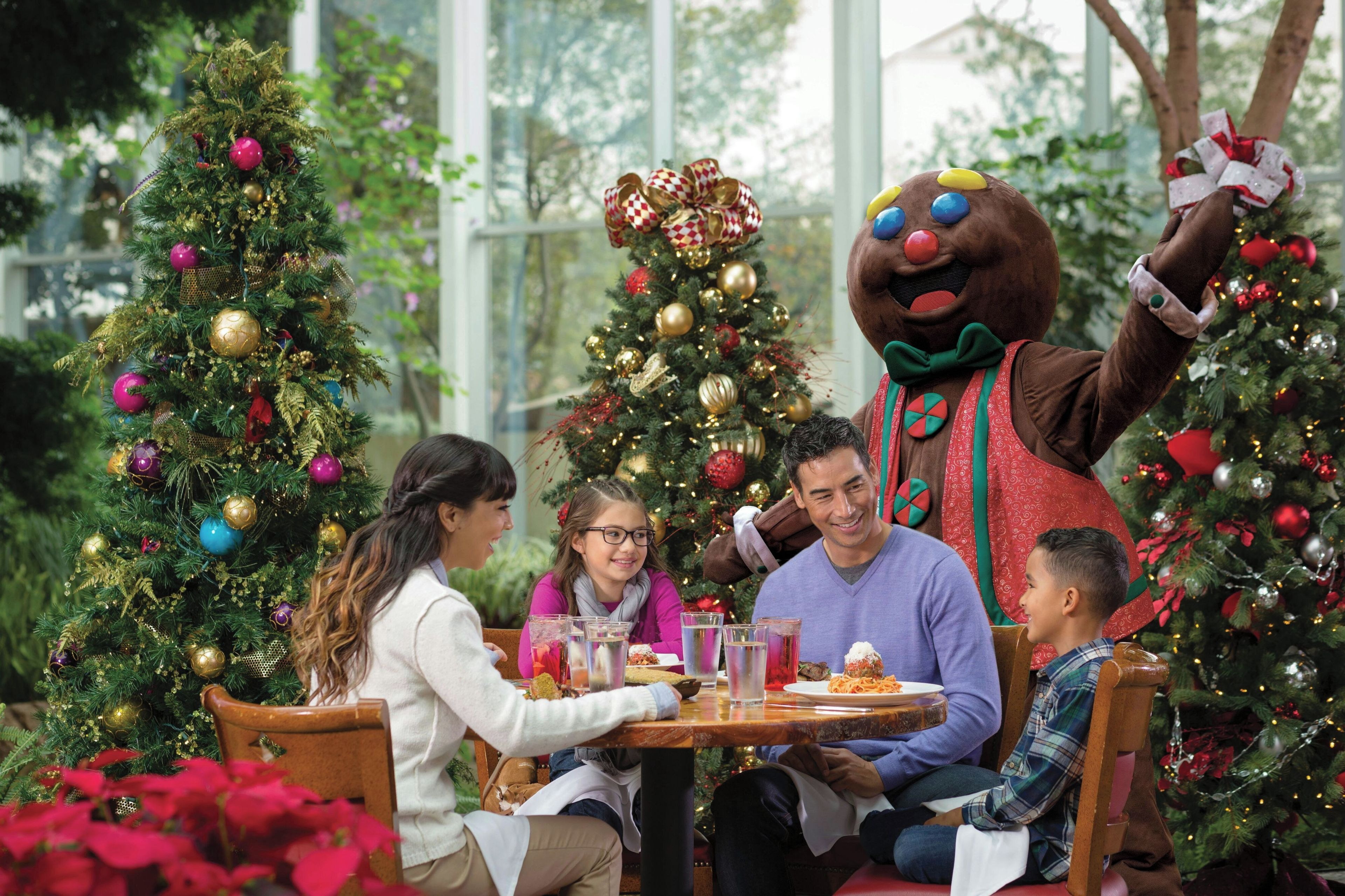 Een gezin dineert buiten, met kerstbomen en een mascotte.