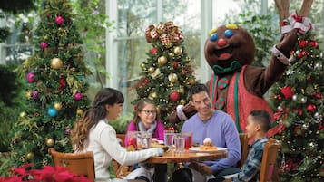 Een gezin dineert buiten, met kerstbomen en een mascotte.