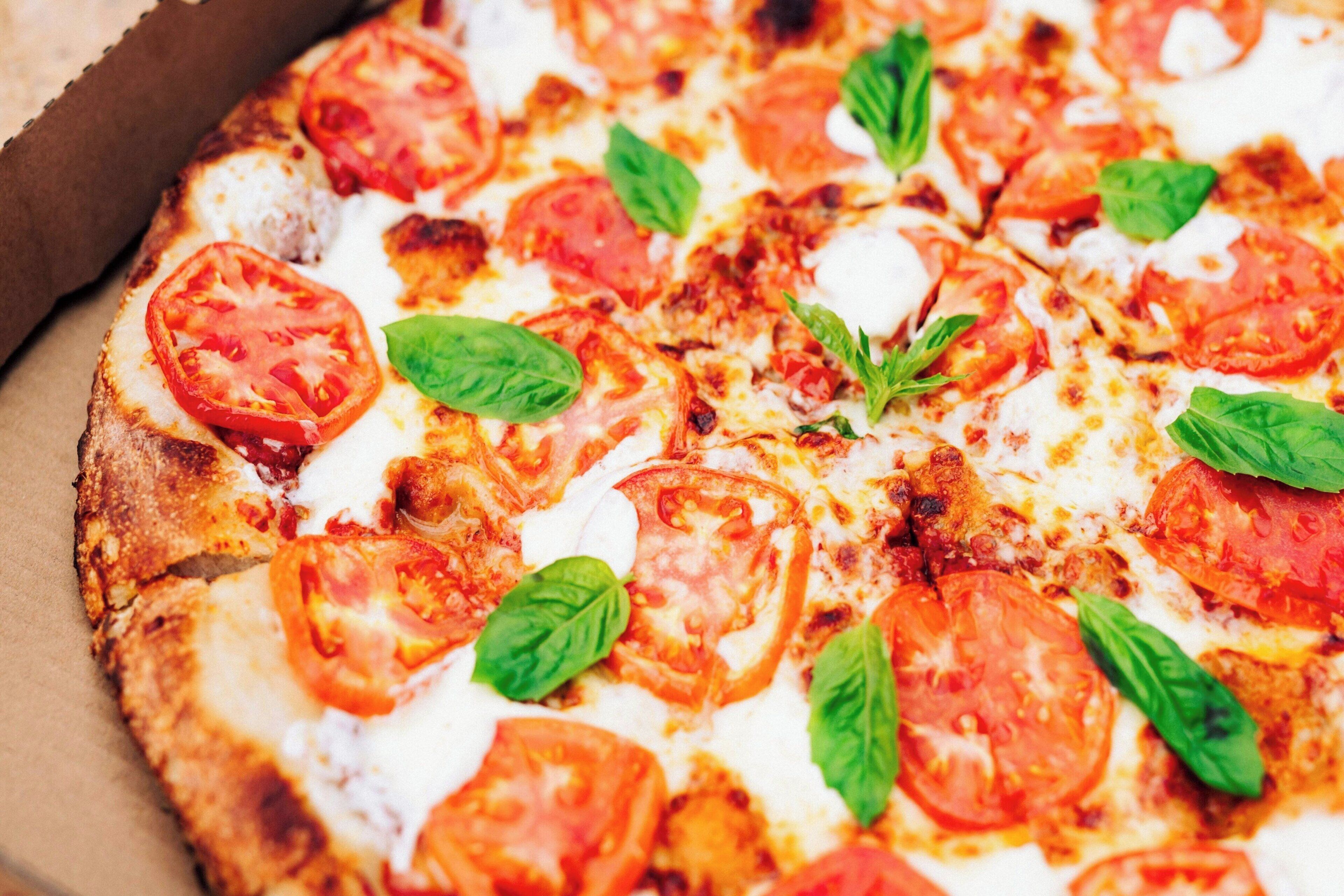 A pizza with tomato slices and basil leaves.