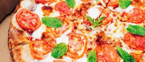Una pizza con rodajas de tomate y hojas de albahaca.
