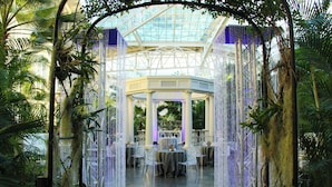 Een binnentuin met glazen dak, tafels met stoelen en hangende decoraties.