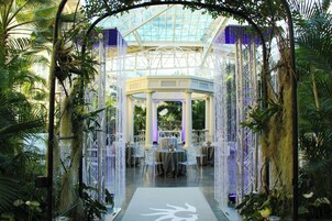 An indoor garden with a glass ceiling, tables with chairs, and hanging decorations.