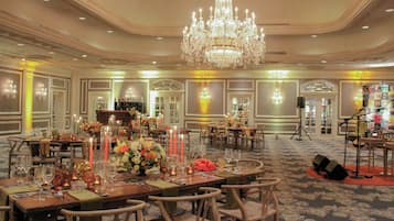 A banquet hall with tables set for dining, a chandelier, and a stage with musical equipment.