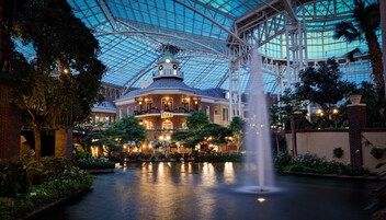 A hotel with a glass ceiling atrium, a fountain, and a river.