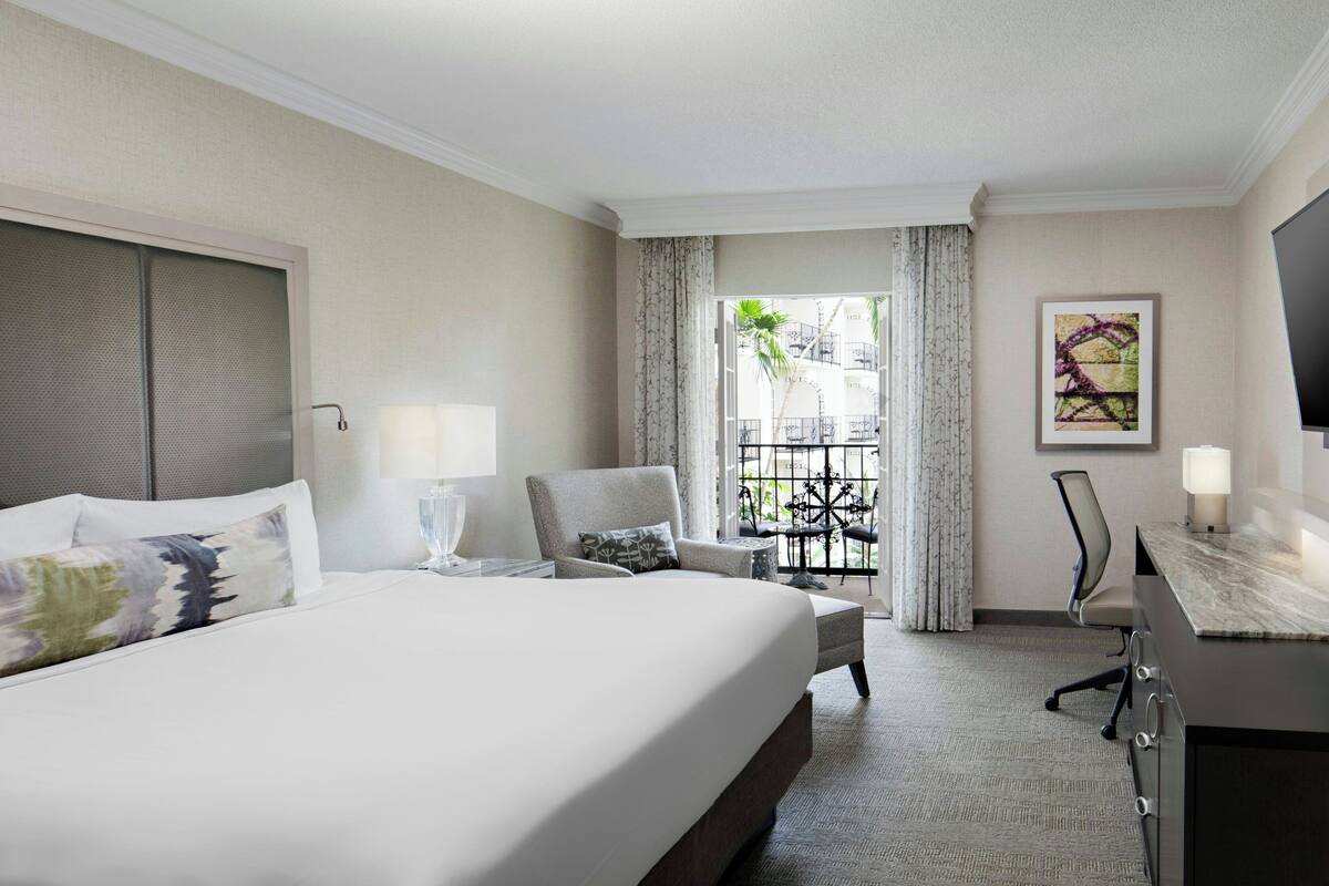 Une chambre d’hôtel avec un grand lit, un bureau, une chaise et une vue sur le balcon extérieur.
