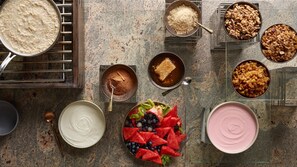 Verschiedene Speisen, darunter Haferflocken, Granola und Joghurt, sowie ein Teller frisches Obst.