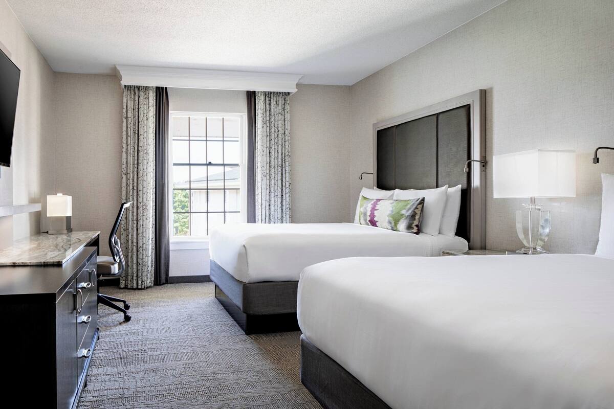 Une chambre d’hôtel avec deux lits, un bureau, une télévision et une fenêtre avec des rideaux.