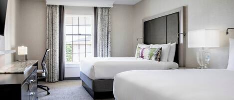 A hotel room with two beds, a desk, a TV, and a window with curtains.