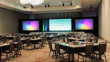 A conference room with multiple tables and chairs, a large screen, and a stage with lighting.