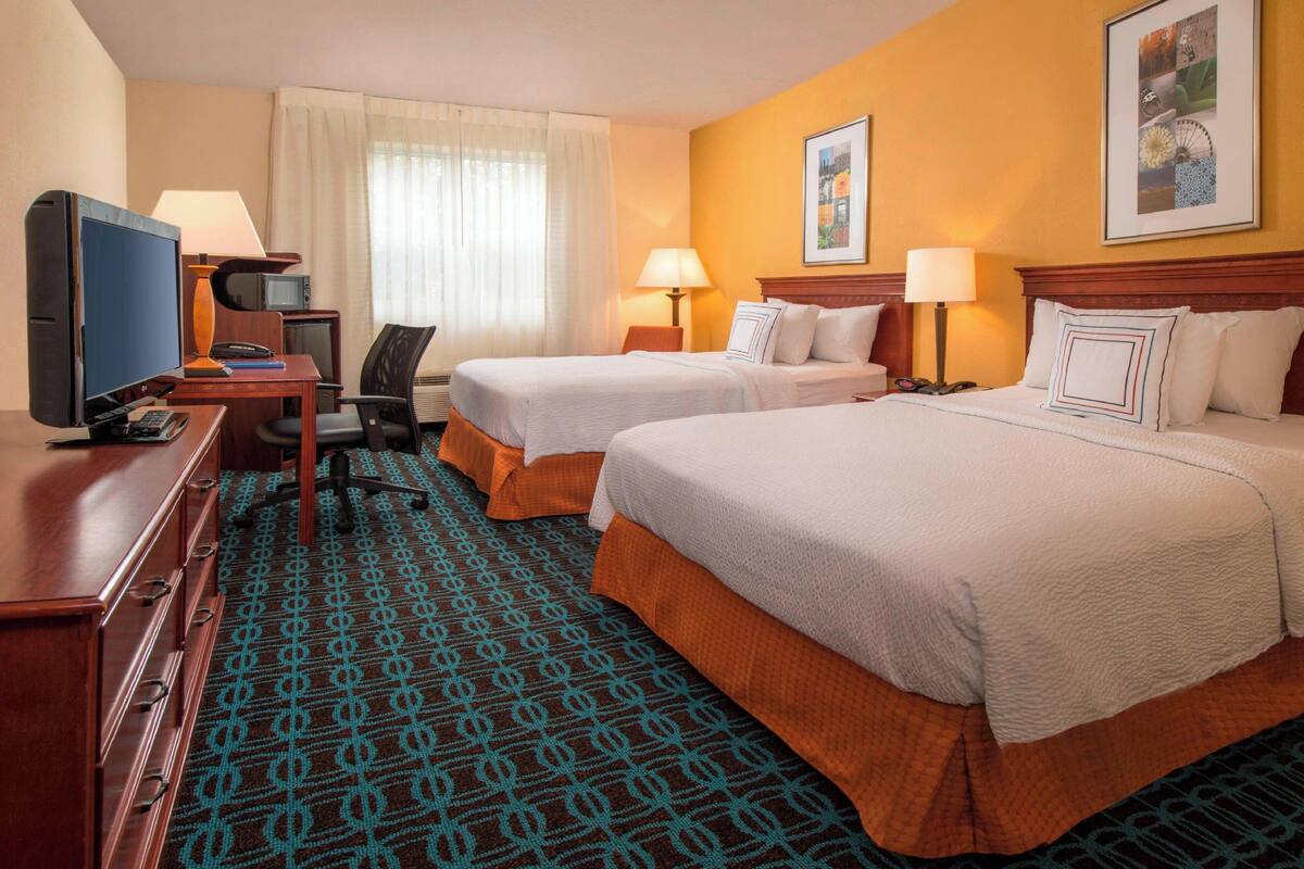 Une chambre d’hôtel avec deux lits, un bureau avec une télévision, une chaise et une moquette à motifs.