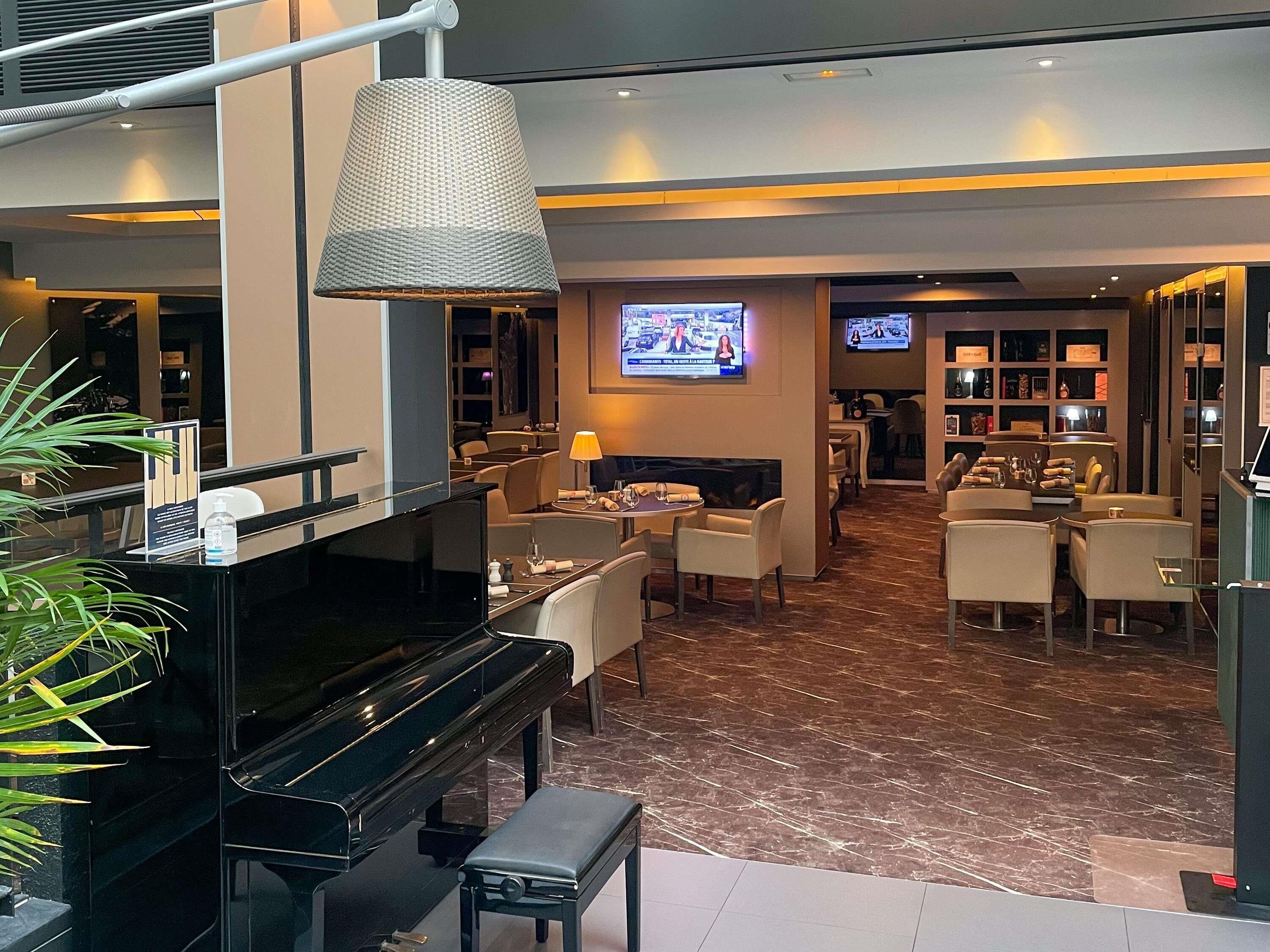 A modern hotel lobby with a piano, seating area, television, and a bar.