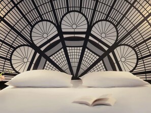 A bed with a geometric patterned headboard, a pillow, and an open book. - Mercure Paris Porte de Versailles Expo (Vanves)
