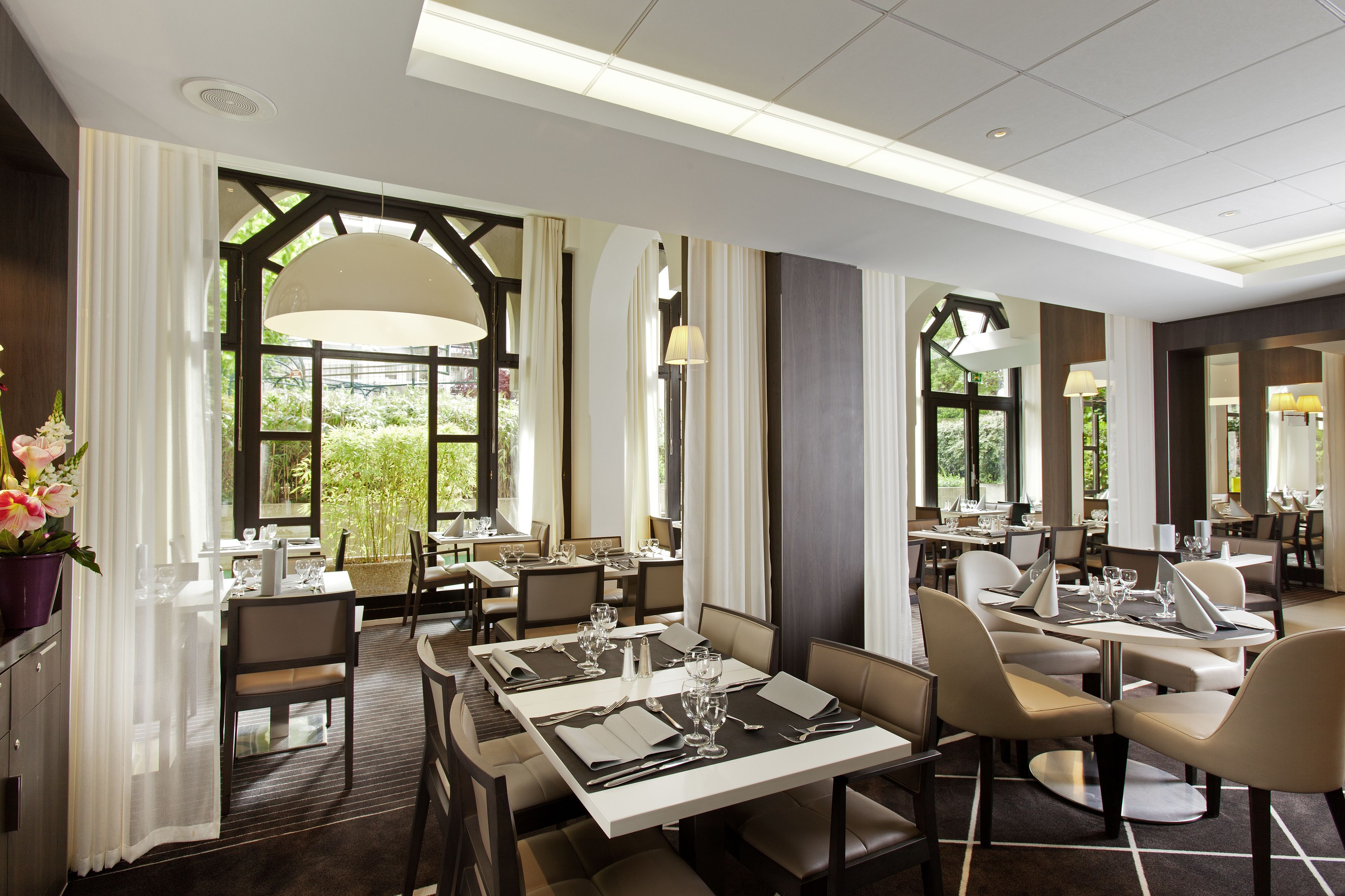 A modern restaurant with multiple dining tables, large windows, and a clean, contemporary interior design.