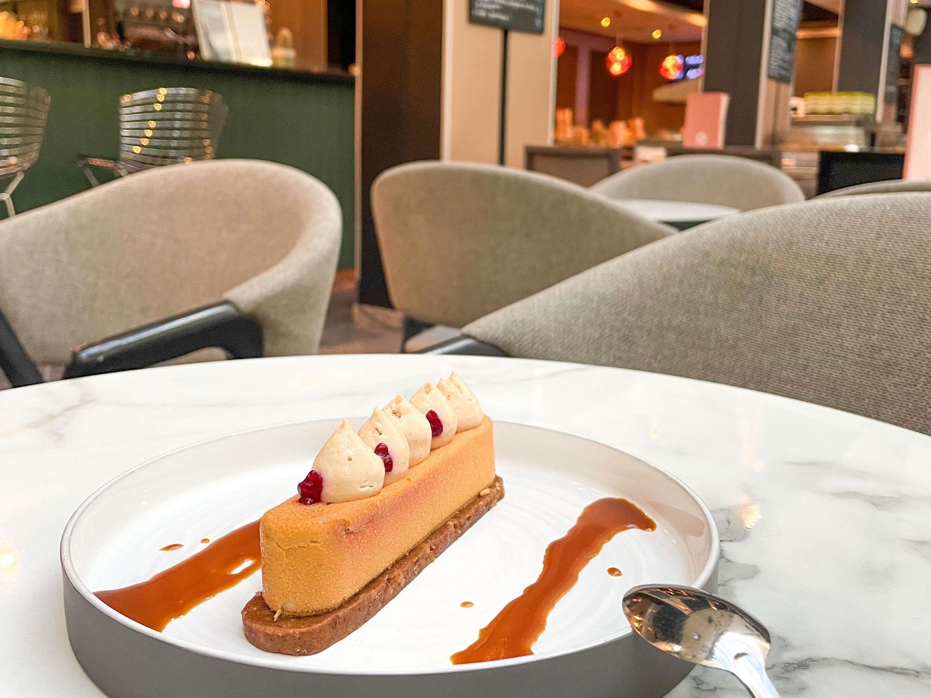 A dessert on a plate with a spoon, set on a marble table in a cafe with chairs and a counter in the background.