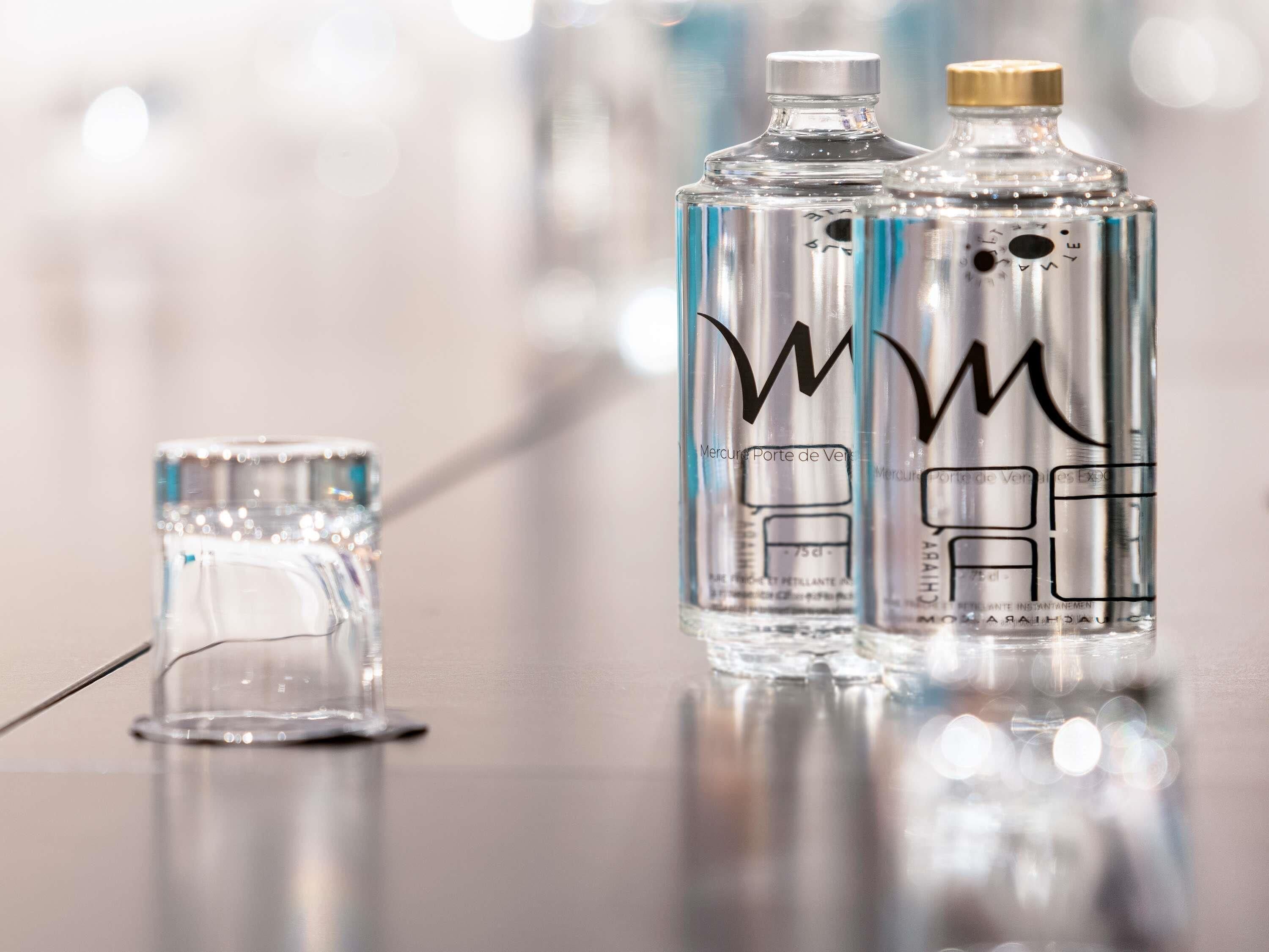 Two clear glass bottles with metallic caps on a reflective surface.