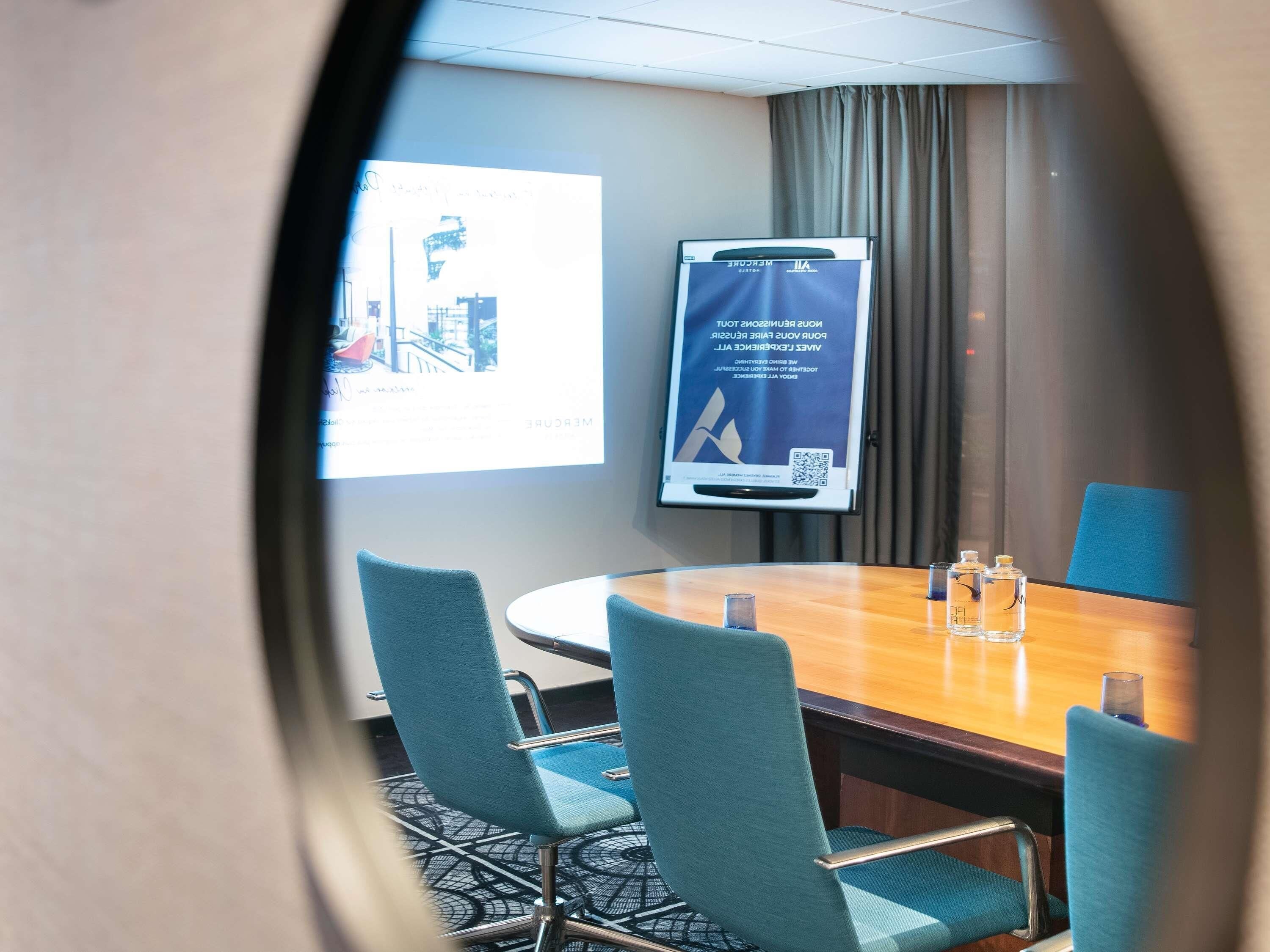 A conference room with a large table, four chairs, a projector screen, and a banner on the wall.