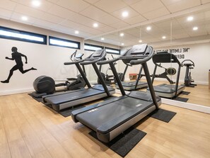 Ein Fitnessraum mit Laufbändern, einer Gewichtbank und einer Spiegelwand.