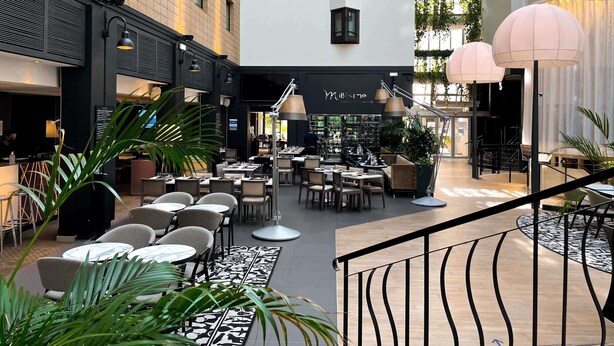 Un patio interior con varias mesas y sillas para comer, una zona de bar y una escalera que lleva a un nivel superior.