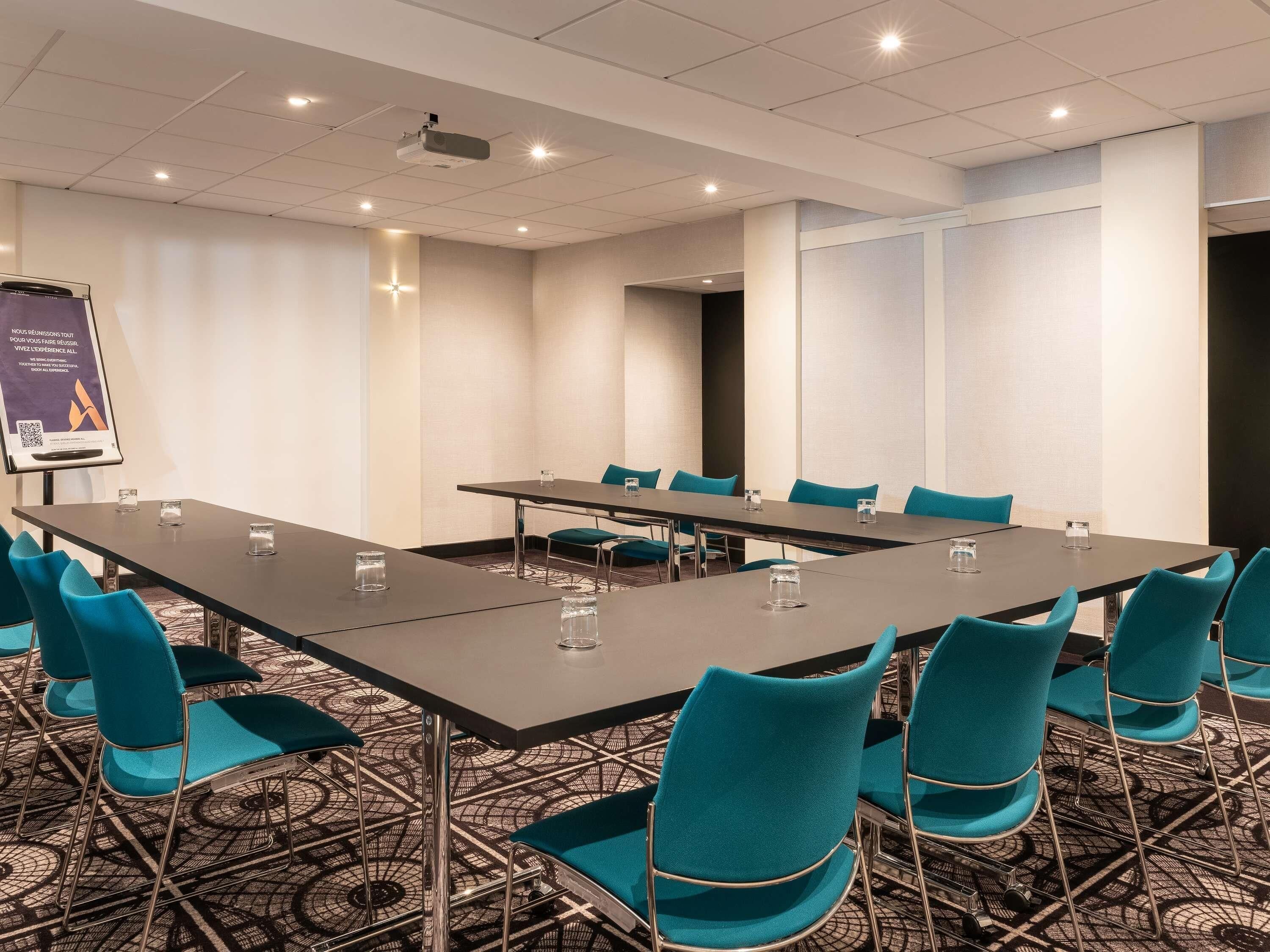 A conference room with a long table, teal chairs, and a projector screen.