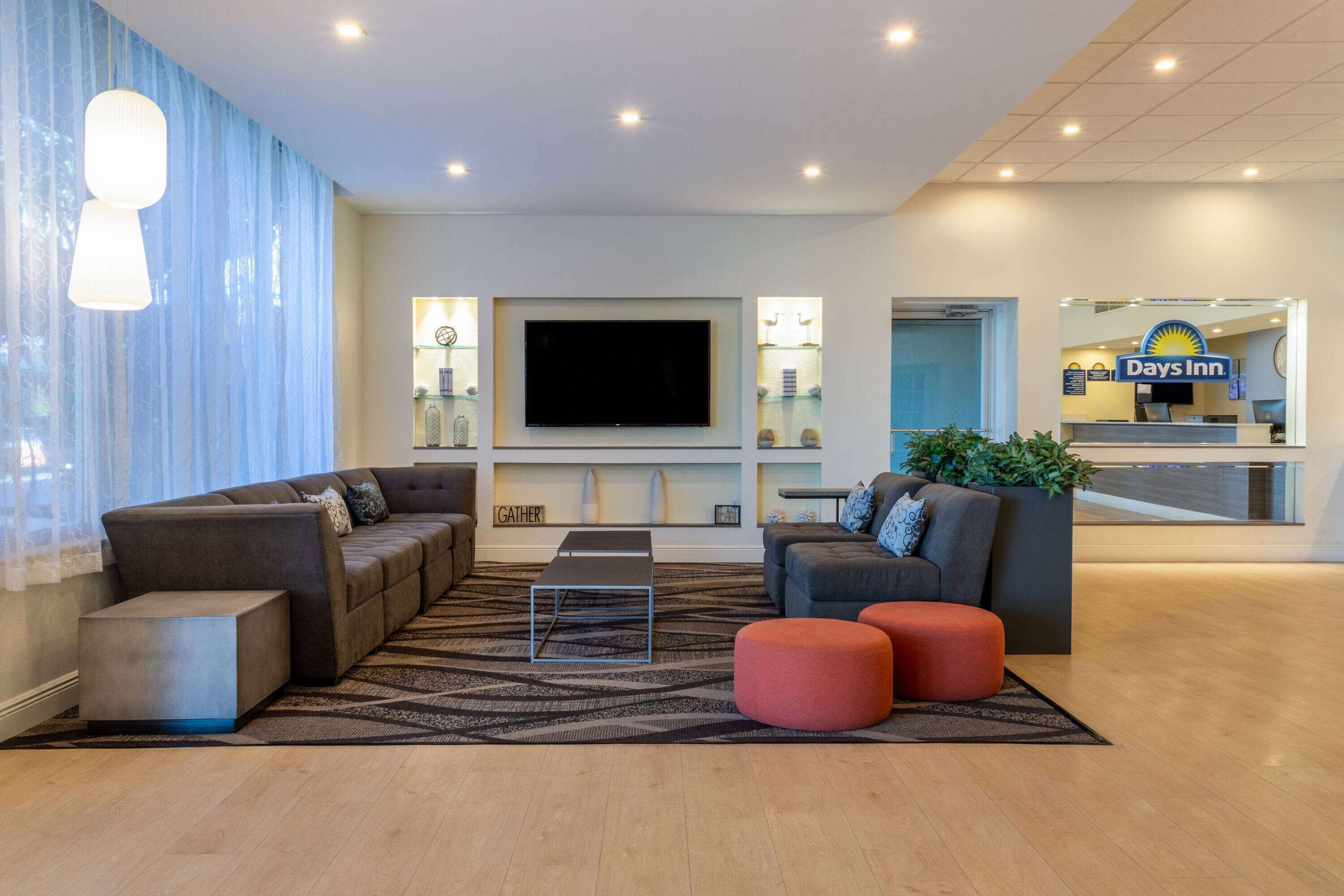 A modern hotel lobby with a large flat-screen TV, comfortable seating areas, and a reception desk.