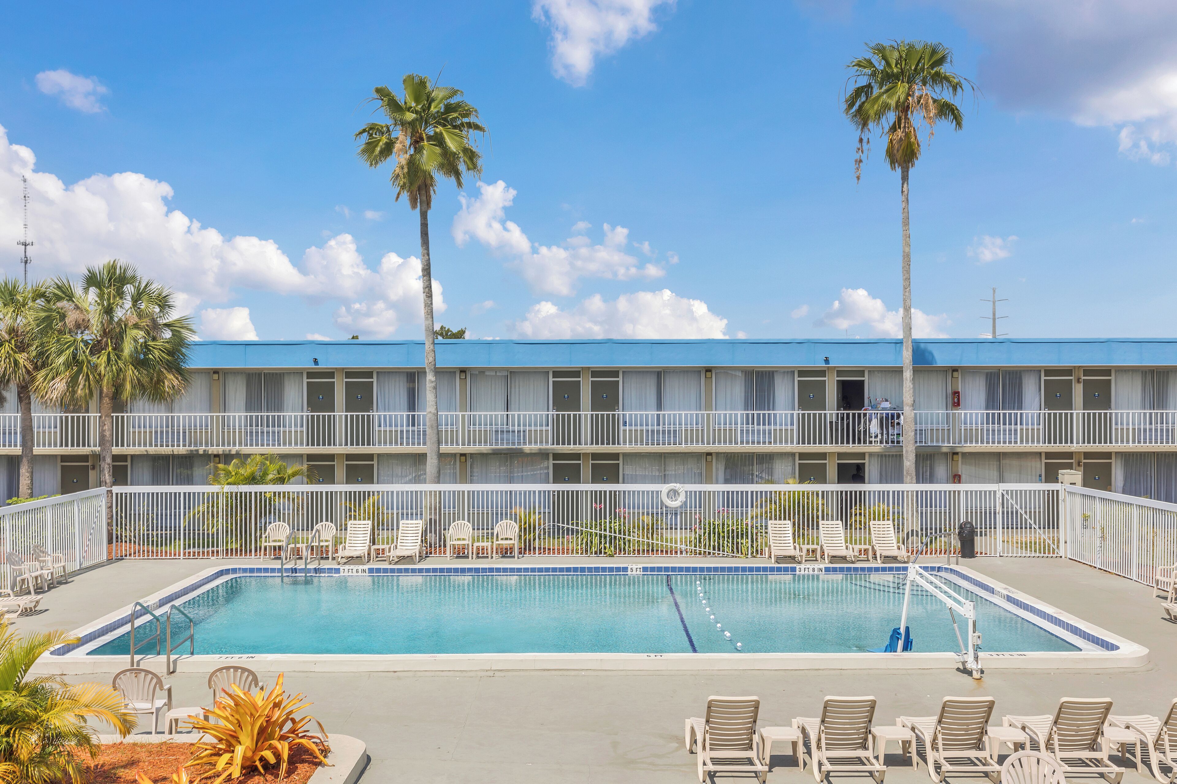 A hotel with a swimming pool, palm trees, and a blue roof.