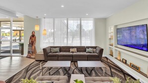 A modern living room with a large sofa, two coffee tables, and a flat-screen TV mounted on the wall. - Days Inn by Wyndham Titusville Kennedy Space Center (Titusville)