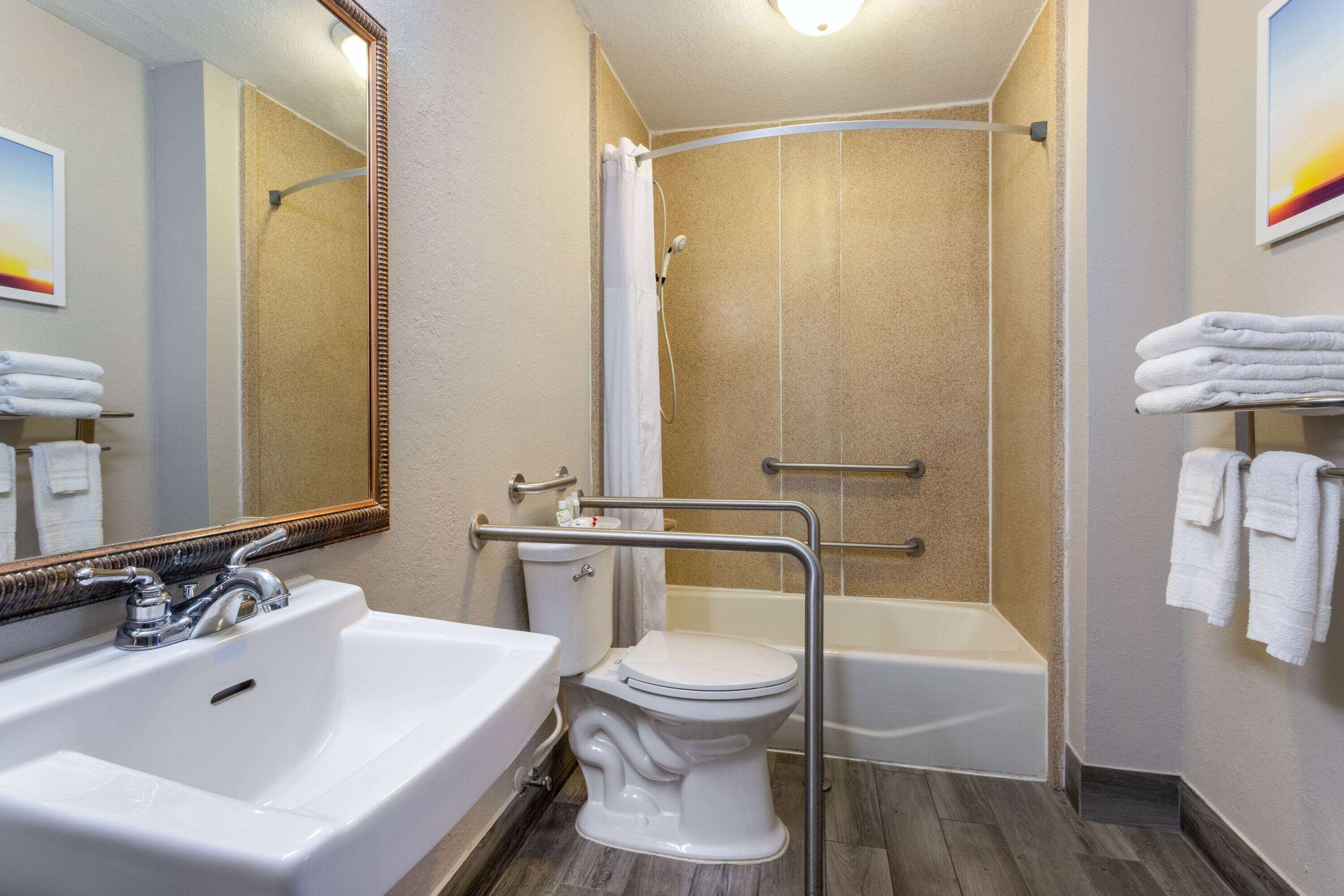 Un baño con lavamanos, inodoro y bañera blancos, ducha con puerta de cristal y espejo con marco de madera.