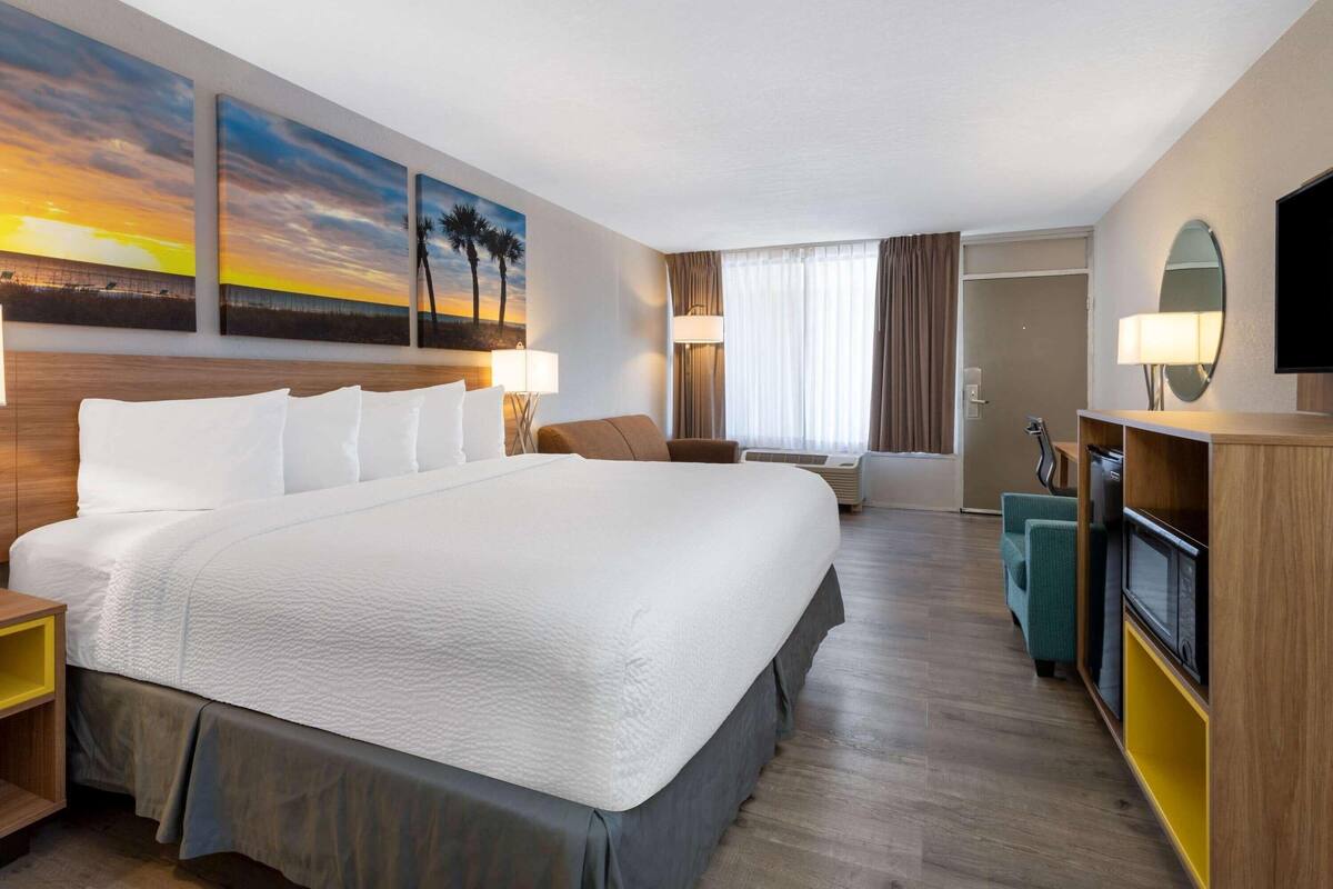 Ein Hotelzimmer mit einem großen Bett, einem Fernseher, einem Schreibtisch und Bildern an den Wänden.