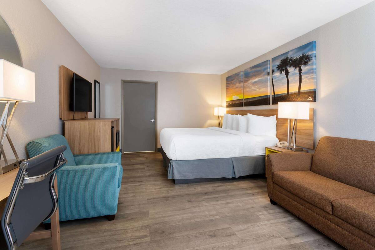 Ein Hotelzimmer mit Bett, Schreibtisch, Sessel, Sofa und einem Bild an der Wand.