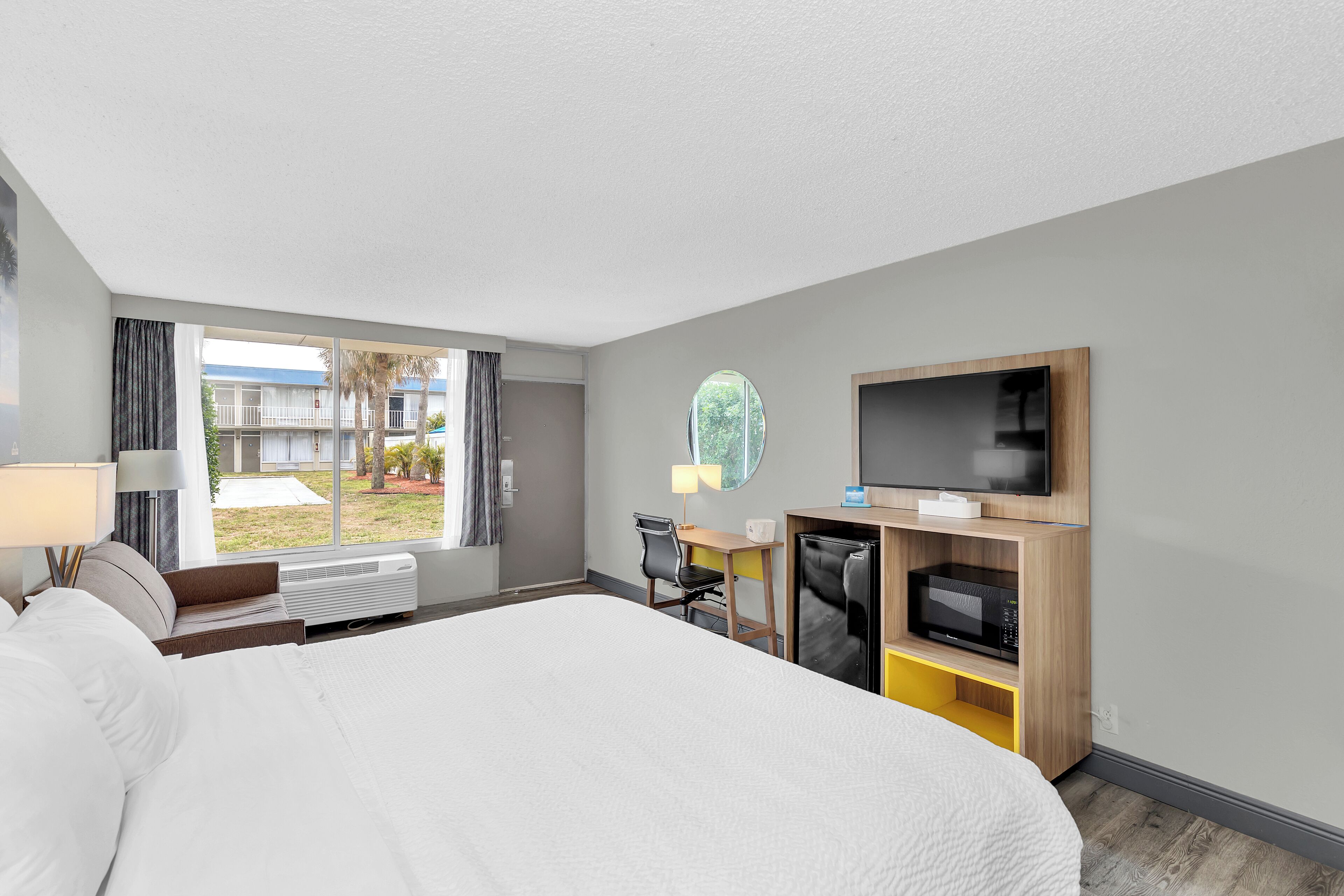 Habitación de hotel con una cama grande, un escritorio con computadora, un televisor y vistas al exterior.