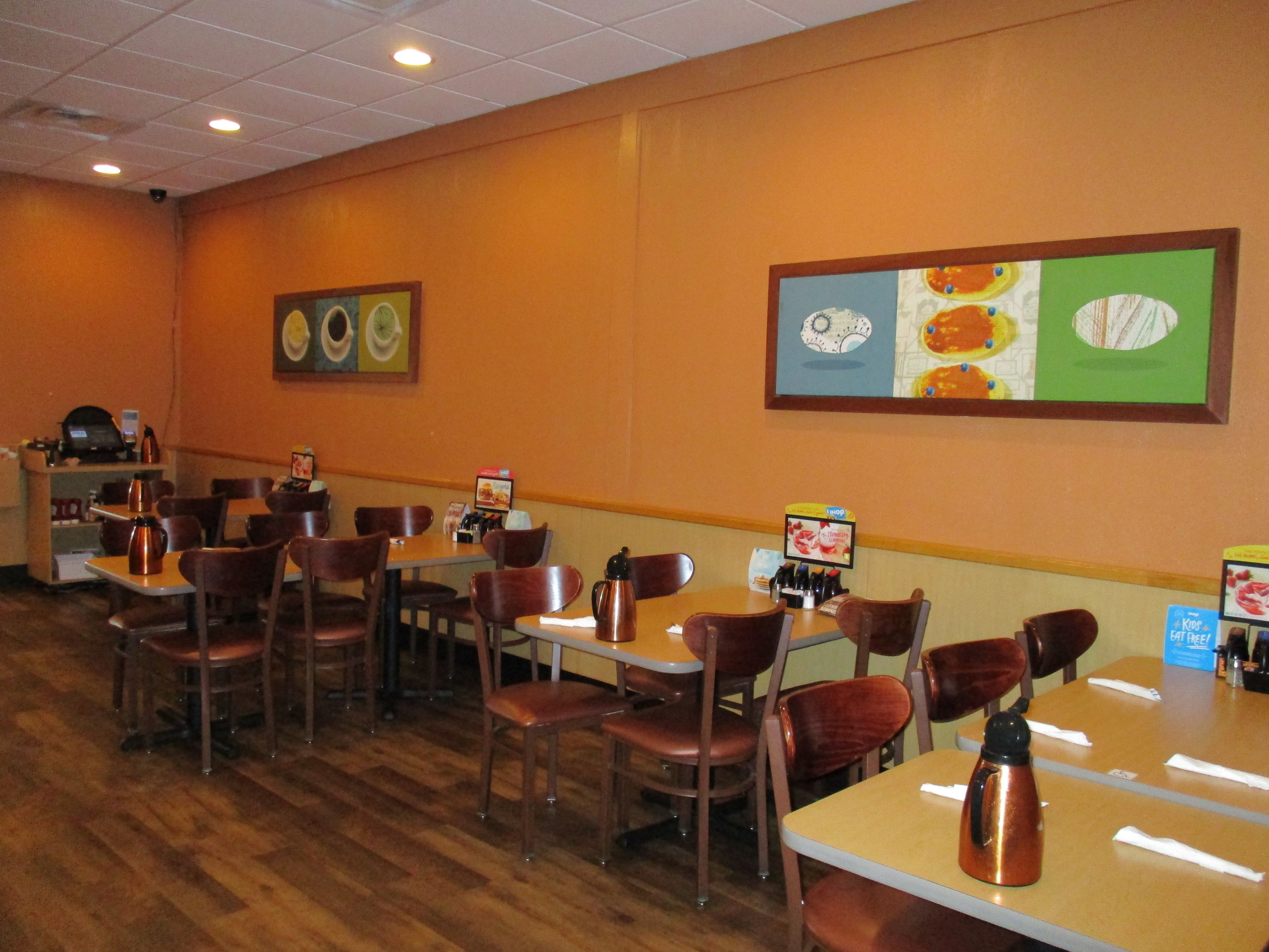 Un restaurant avec des tables et des chaises en bois, un coin café et des œuvres d’art murales représentant des aliments.