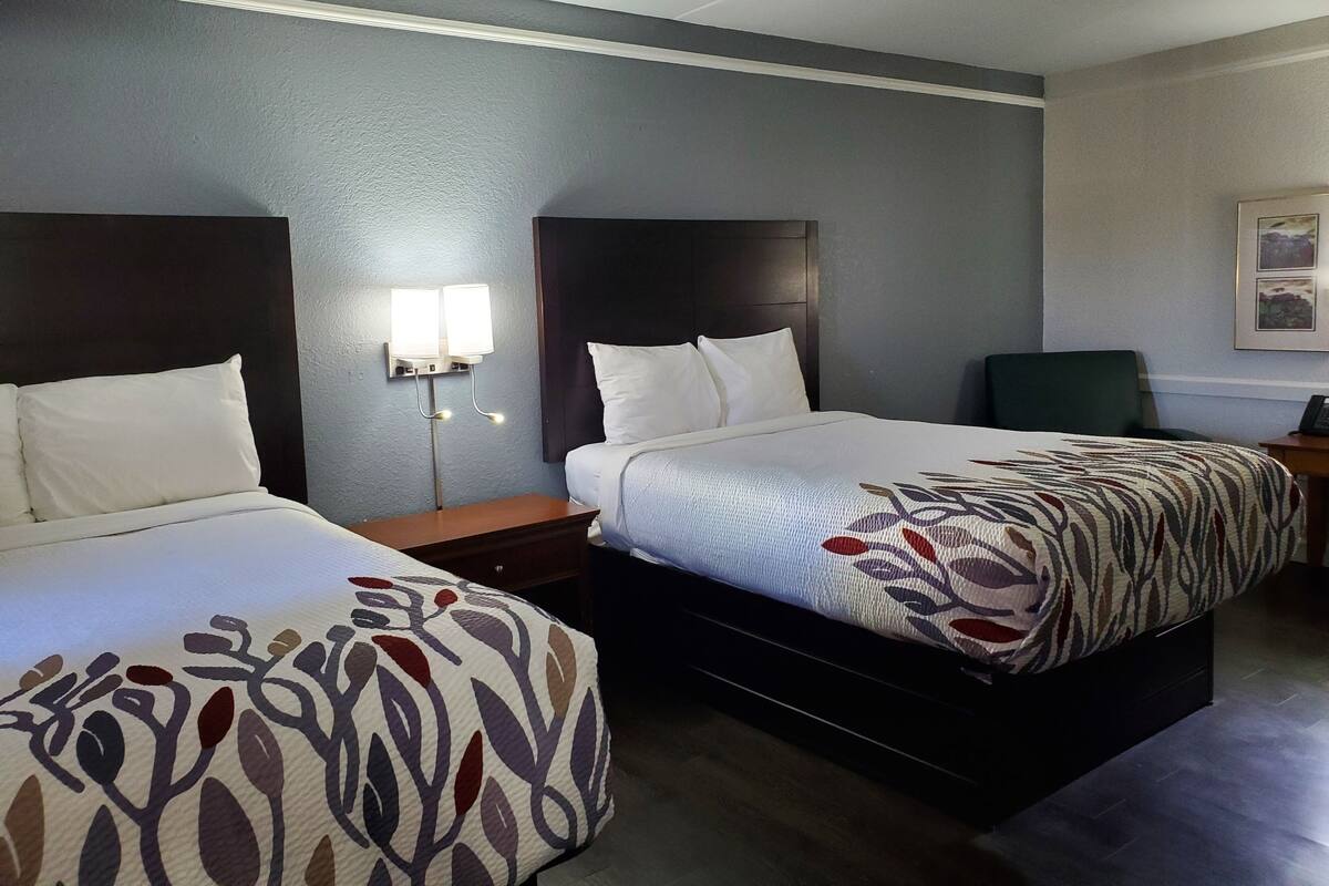 A hotel room with two beds, a nightstand with a lamp, and a framed picture on the wall.