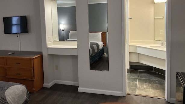 Ein Hotelzimmer mit Bett, Fernseher, Kommode und Bad mit Waschbecken und Spiegel.