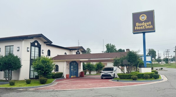 A Budget Host Inn with a red-bricked entrance, a covered parking area, and a large signboard. - Budget Host Inn- Medical Center (Little Rock)