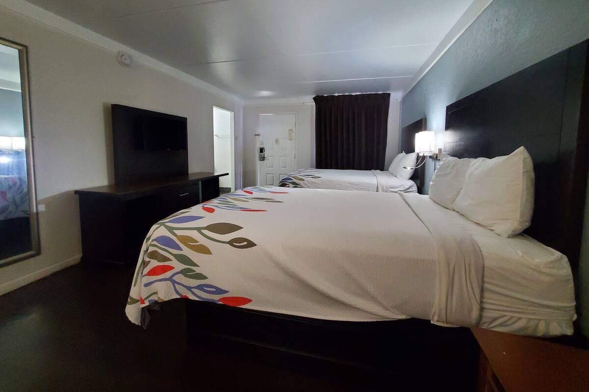 A hotel room with a large bed, a TV mounted on the wall, a desk, and a door leading to another room.