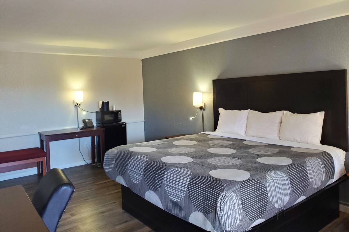 A hotel room with a bed, bedside lamps, a desk with a chair, and a small table with a telephone.
