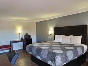 A hotel room with a bed, bedside lamps, a desk with a chair, and a small table with a telephone. - Budget Host Inn- Medical Center (Little Rock)