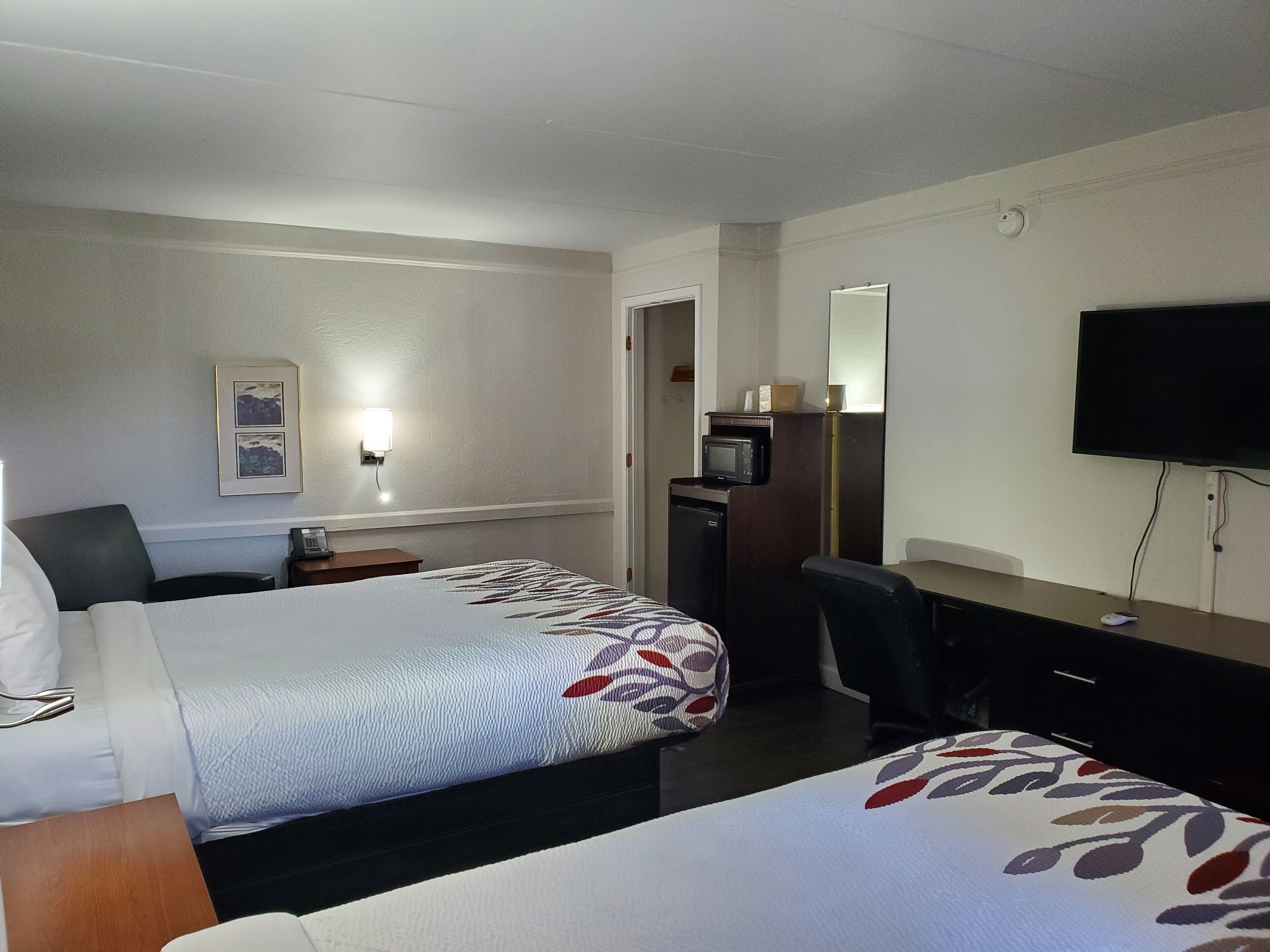Ein Hotelzimmer mit zwei Betten, einem Schreibtisch, einem Computer, einem Fernseher und einer Mikrowelle.