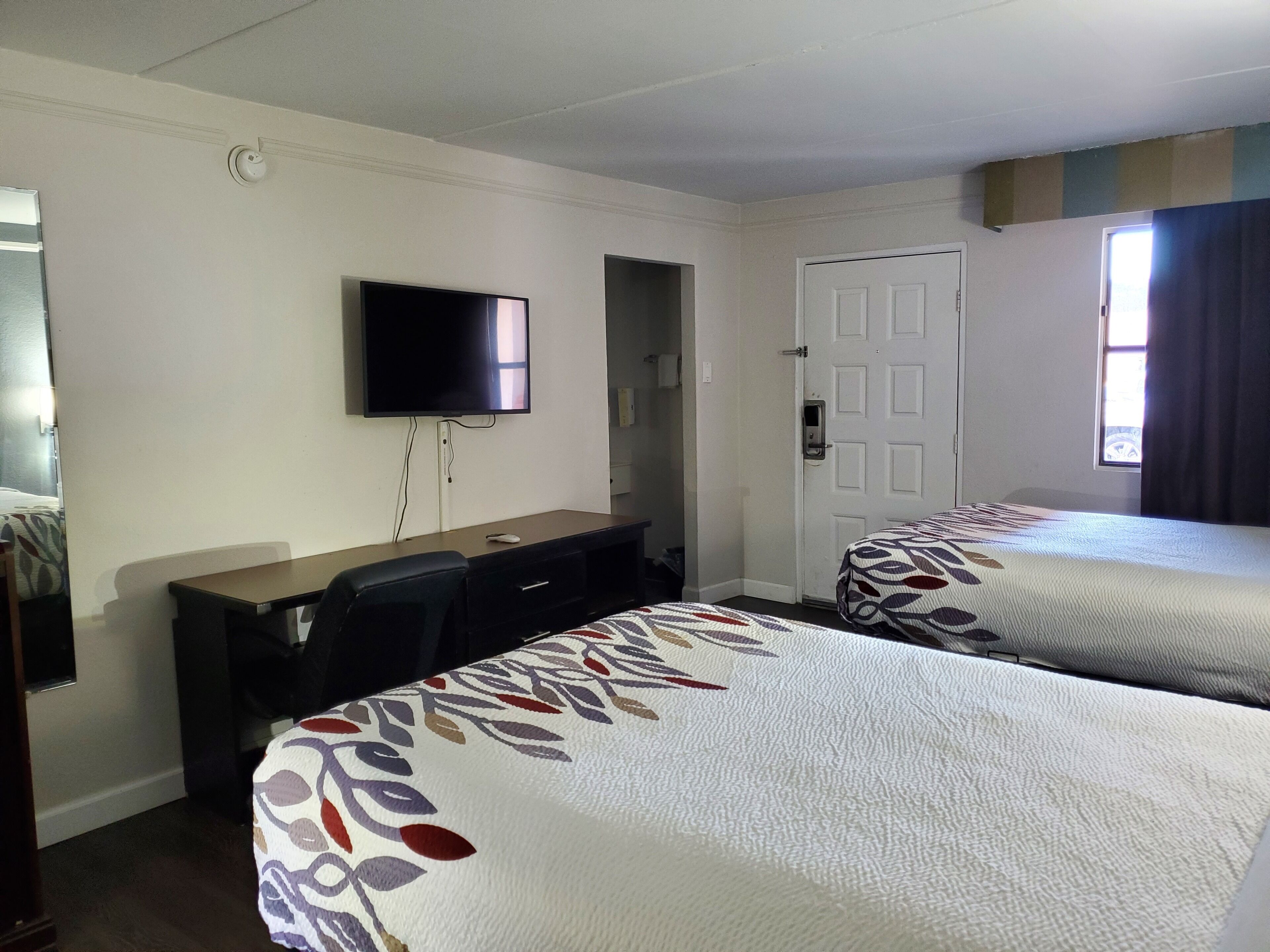 Une chambre d’hôtel avec un lit, un bureau, une télévision et une porte.