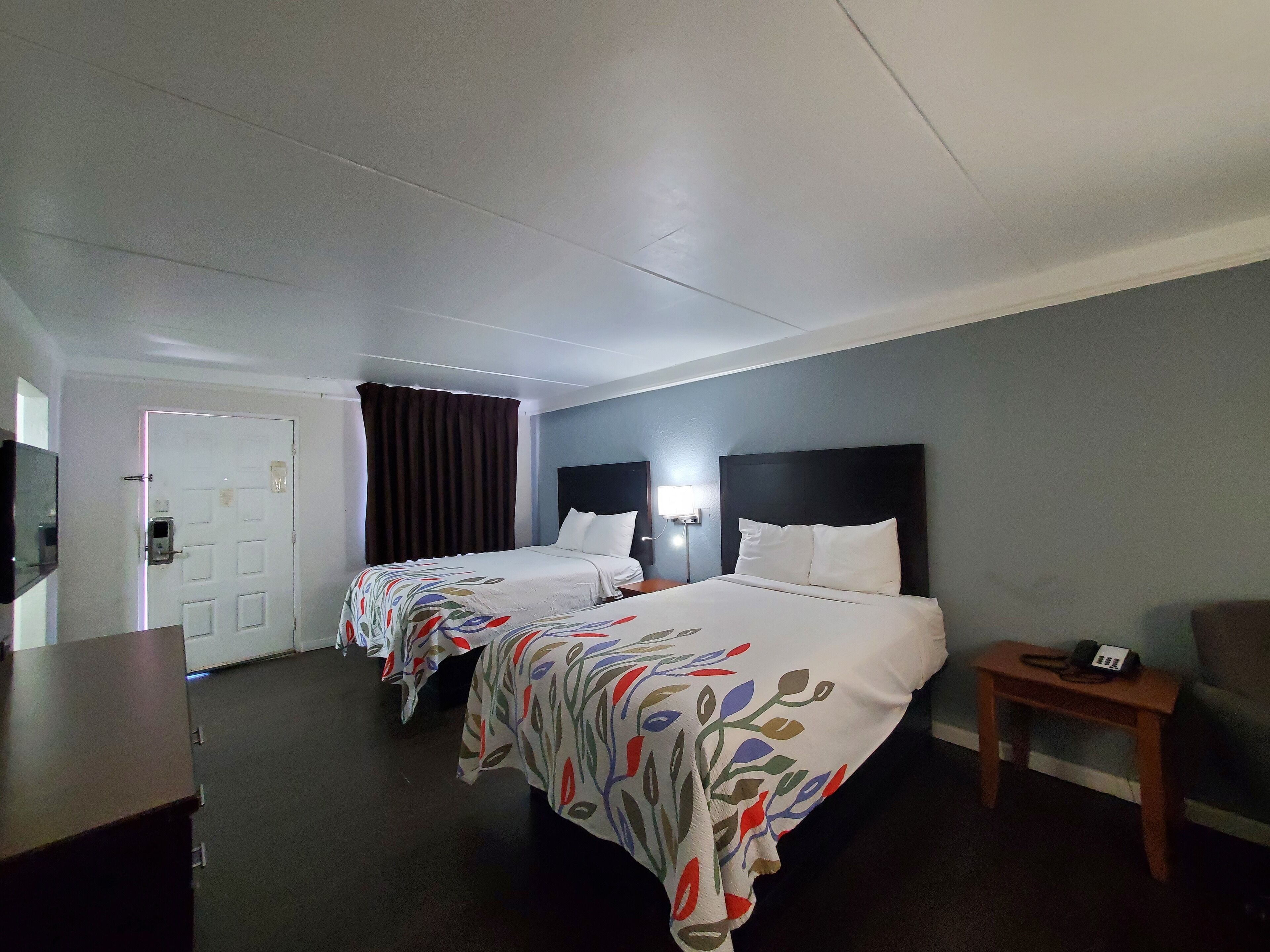 A hotel room with two beds, a desk, a chair, and a bedside table with a phone.