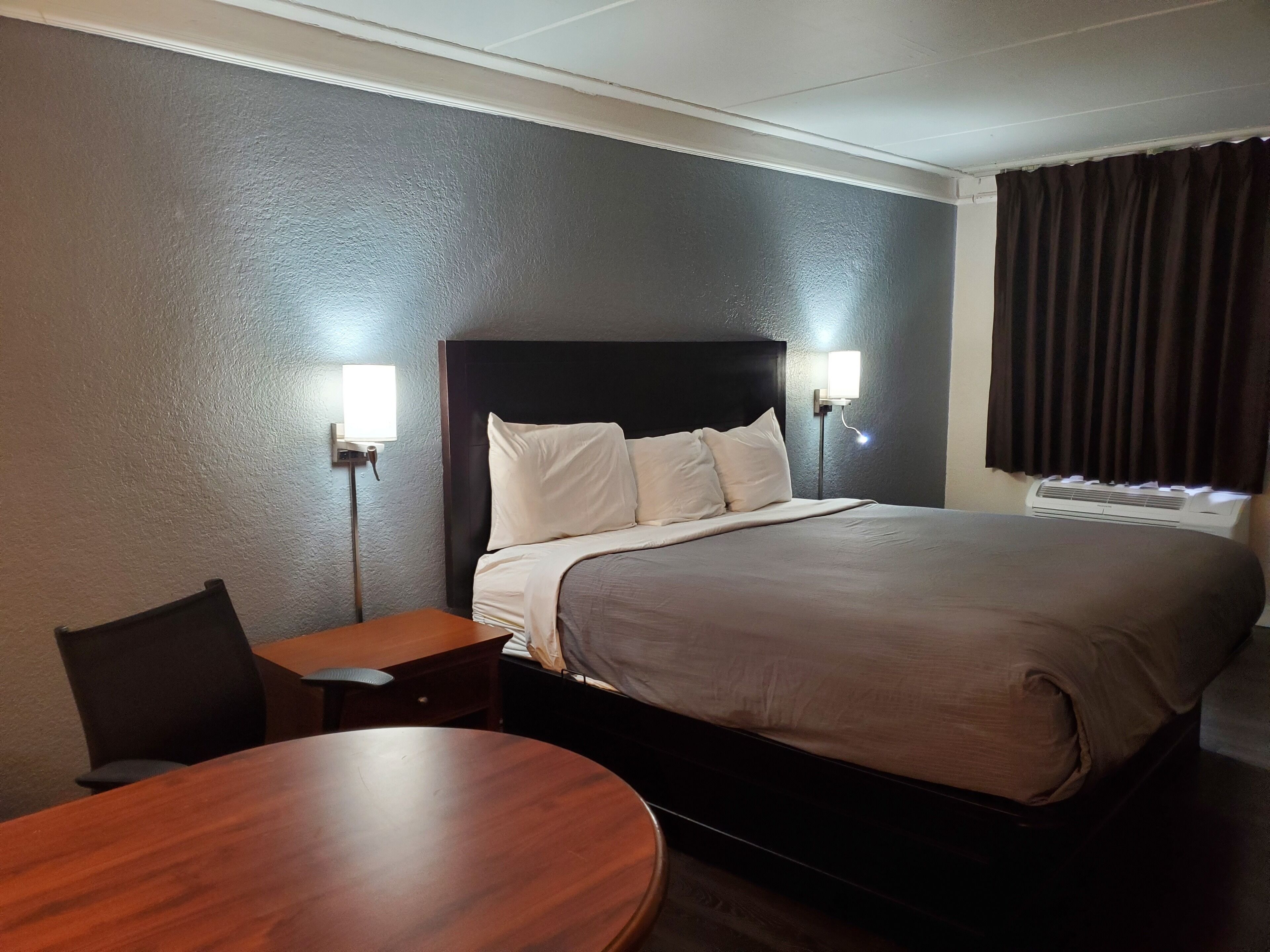A hotel room with a large bed, two bedside lamps, a wooden nightstand, and a round wooden table.