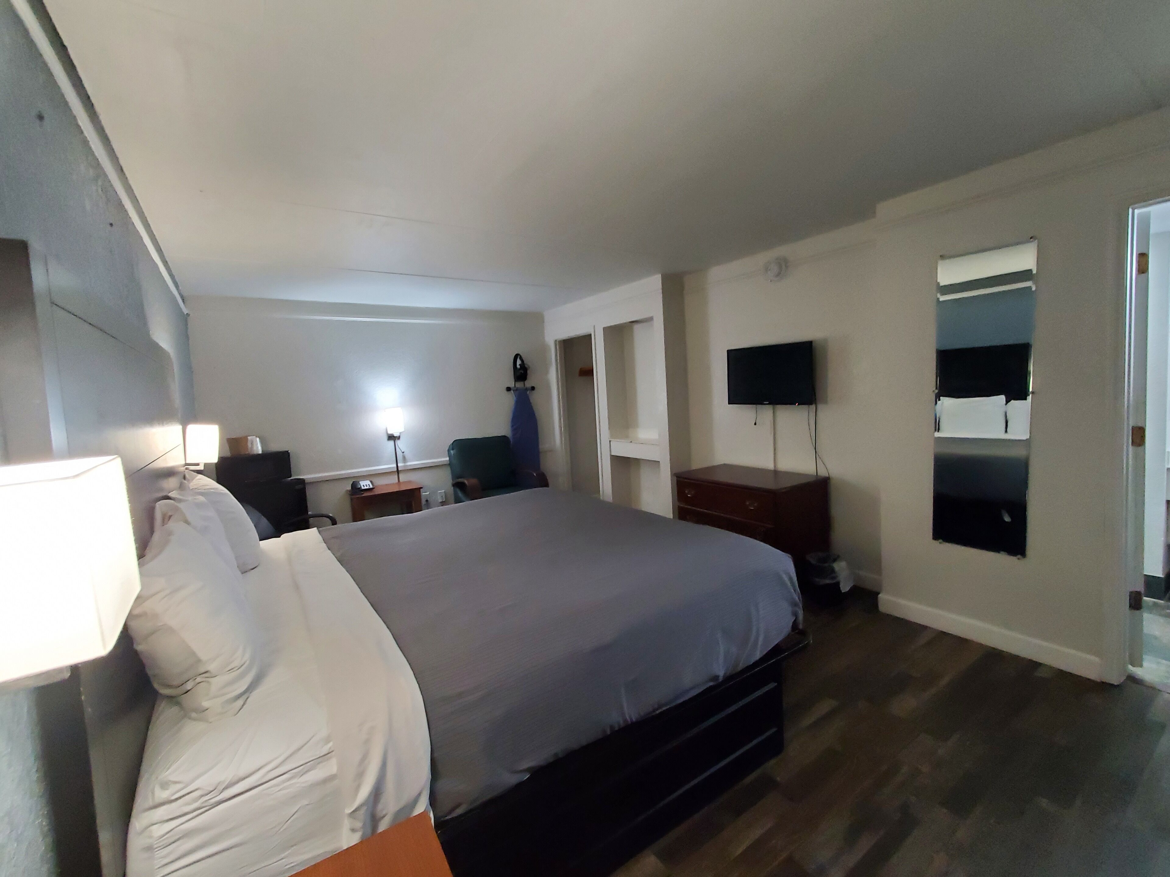 A hotel room with a large bed, a desk with a lamp, a chair, a TV mounted on the wall, and a small window.