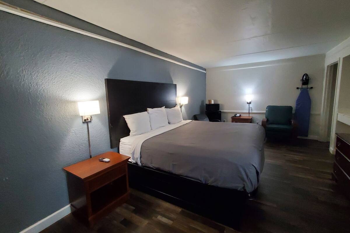 A hotel room with a large bed, bedside tables, a desk, a chair, and a lamp.