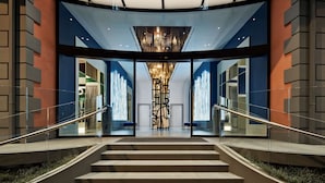 A modern building entrance with a glass facade, a central chandelier, and a staircase leading to the upper floor. - De Bonart Naples, Curio Collection by Hilton (Naples)