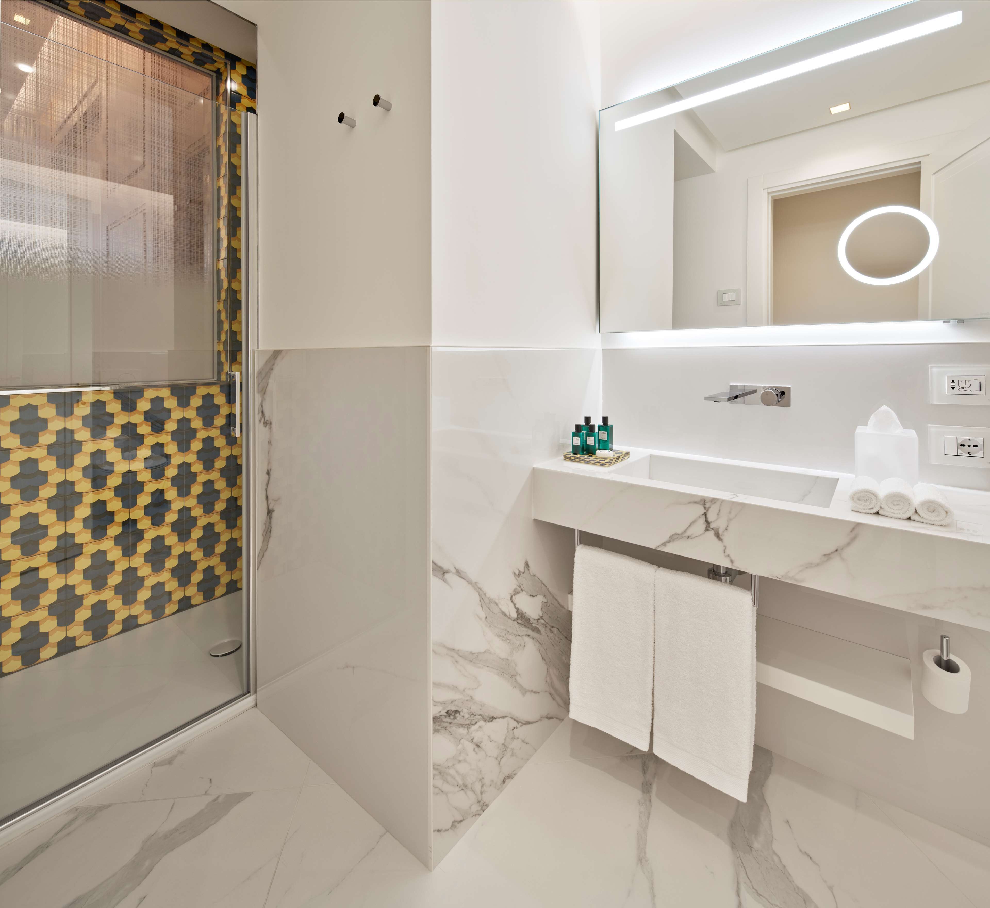 Een moderne badkamer met een glazen douchecabine, een marmeren vloer, een wit wastafelmeubel met spiegel en een handdoekhouder.