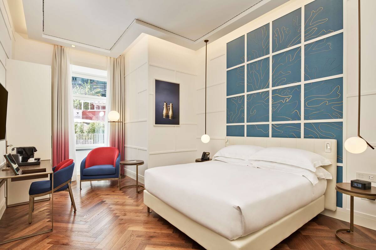 A hotel room with a large bed, a desk with a laptop, a chair, and a view of the outdoors.