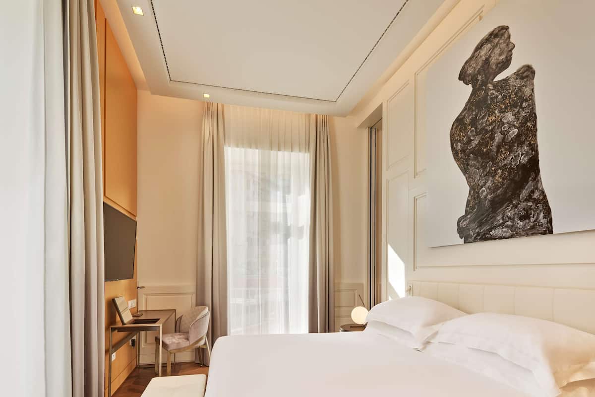A hotel room with a large bed, a desk, a chair, and a painting on the wall.