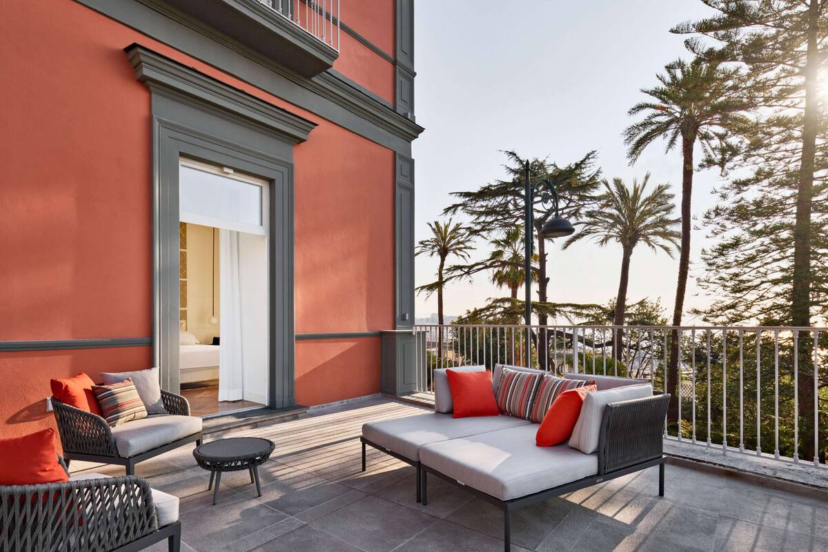 A modern outdoor seating area with a sofa and chairs, a small round table, and a balcony with a railing.