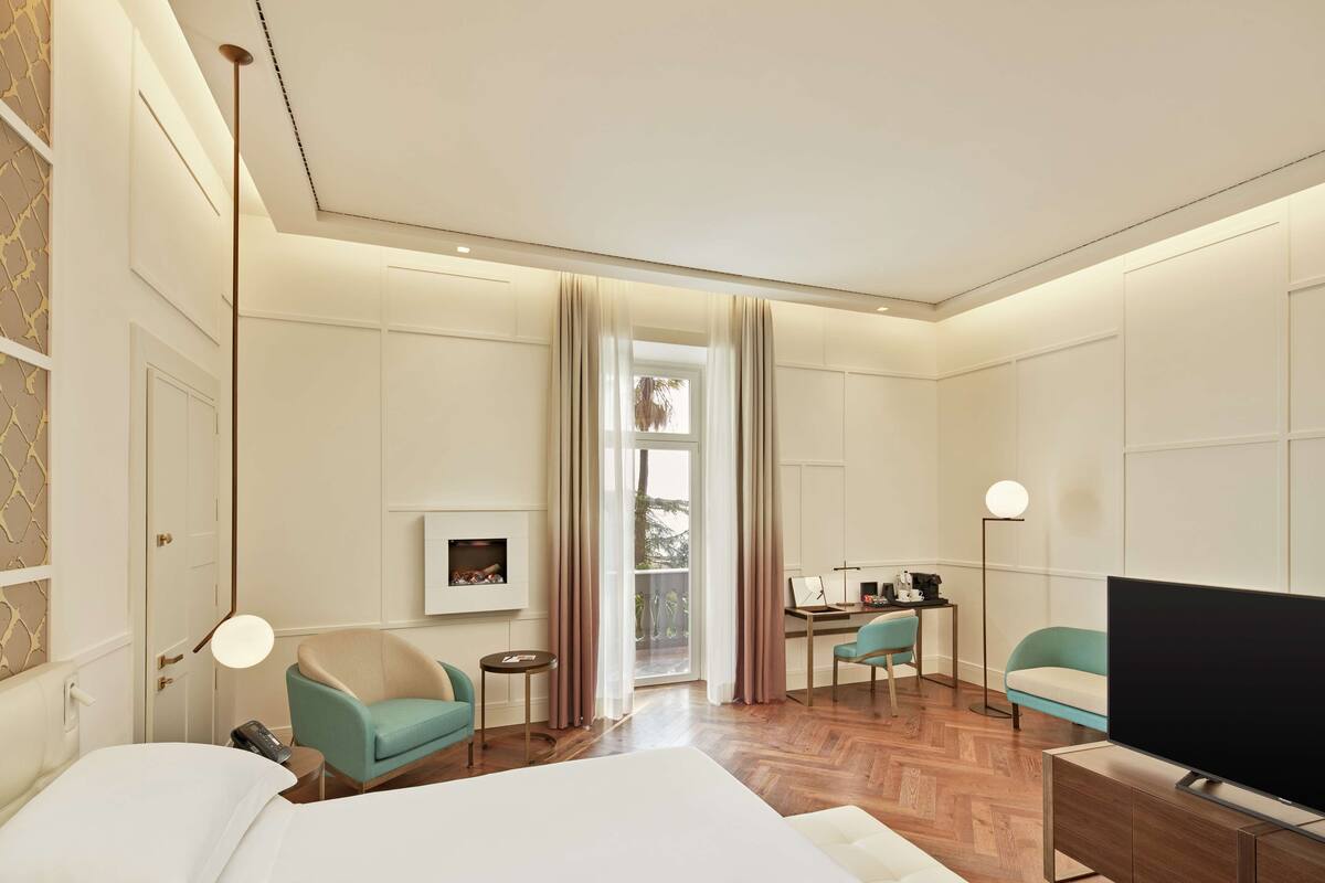 A modern hotel room with a large bed, a desk, a TV, and a view of the outdoors.