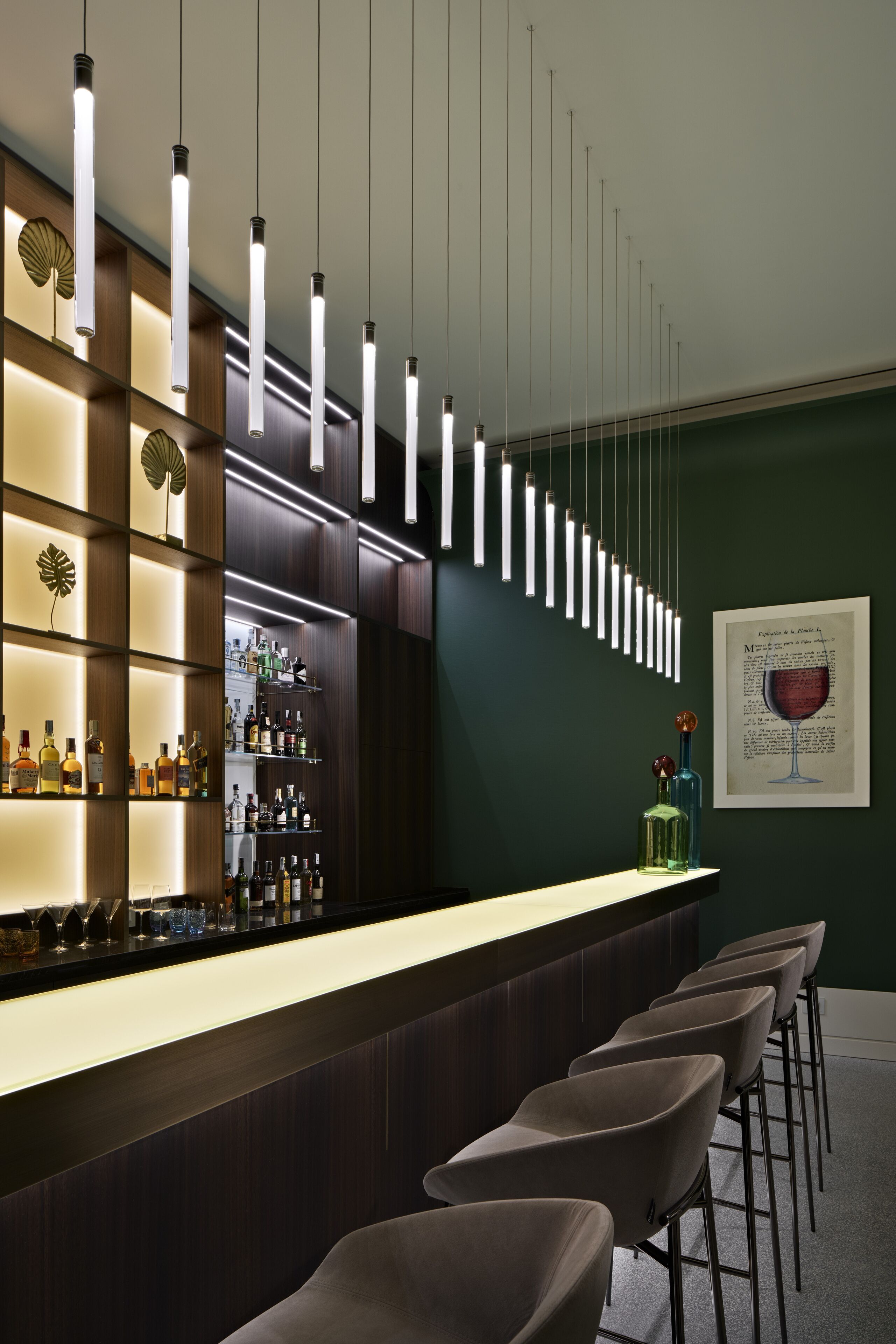Eine Bar mit einer langen Theke, mehreren Flaschenregalen, hängenden Pendelleuchten und einer gerahmten Speisekarte an der Wand.